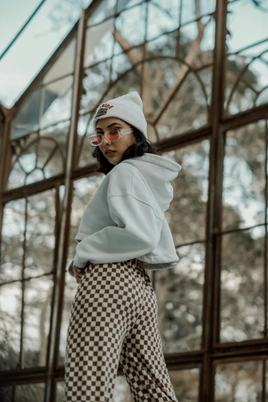 woman with hat and checkered pants standing by glass