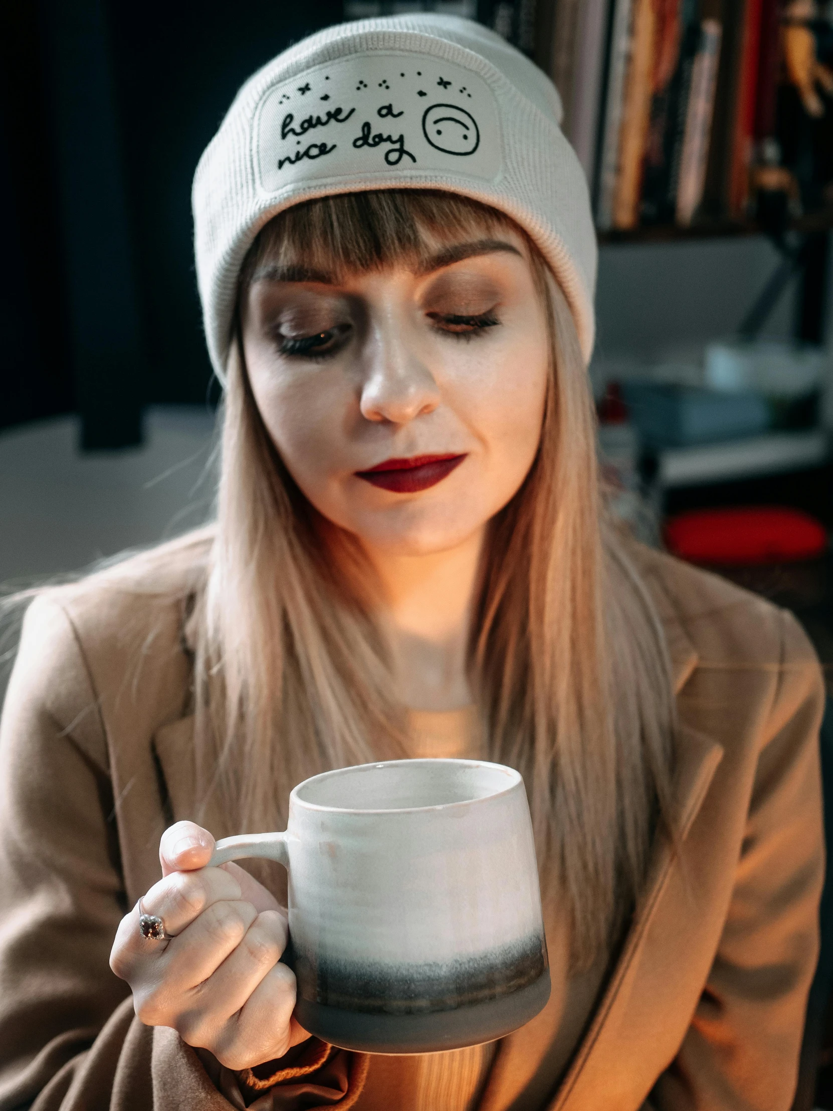 a woman is holding a cup with her hands and a hat on