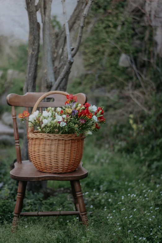 a basket filled with flowers sitting on top of a wooden chair