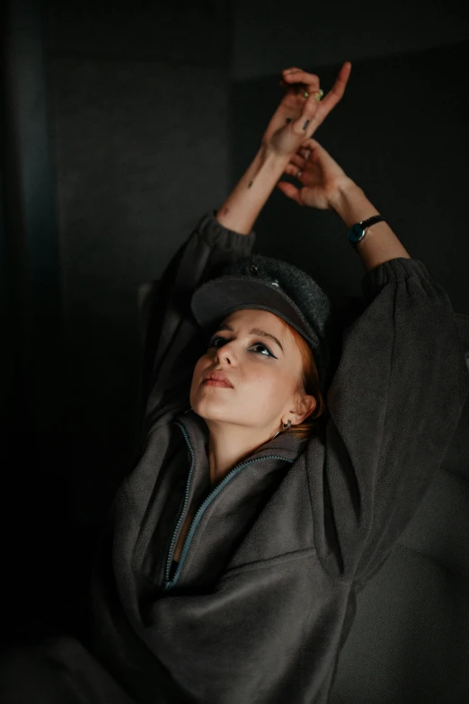 a woman in a gray coat and black hat holds up her hand to the sky