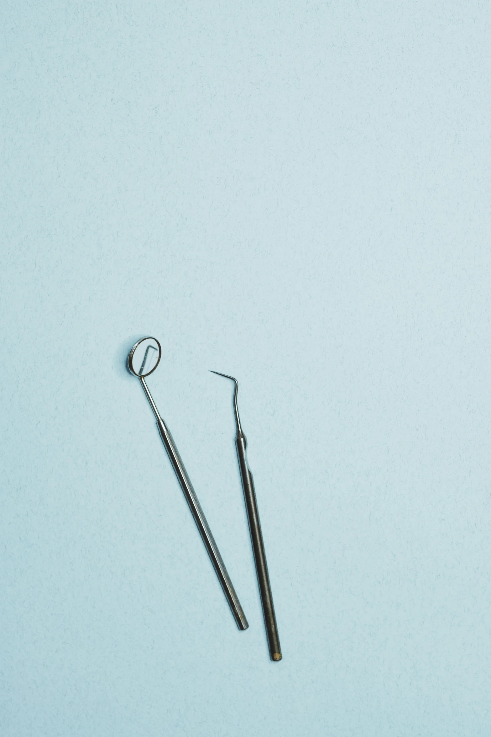 a pair of dental instruments laying side by side on a light blue surface