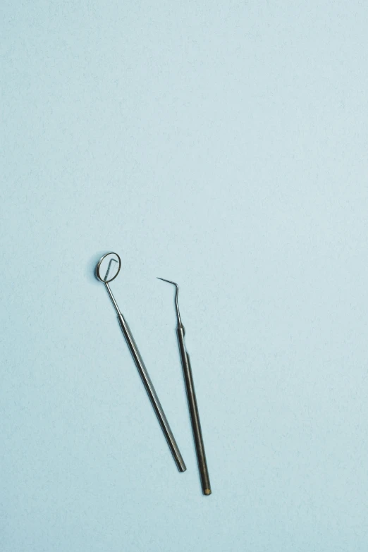 a pair of dental instruments laying side by side on a light blue surface