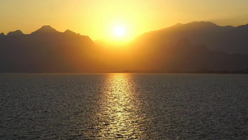 the sun sets over water, mountains behind them