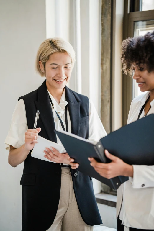 two women at a desk smiling with one holding a clip board and pen