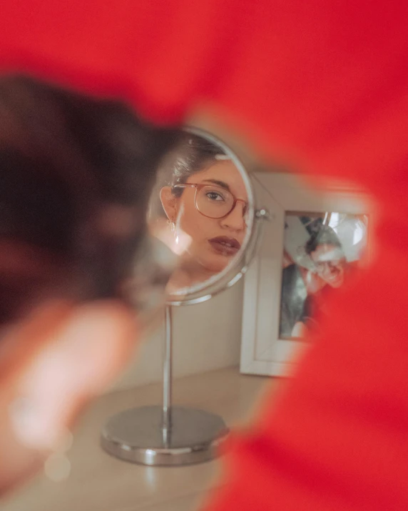 a woman with glasses looks into a mirror