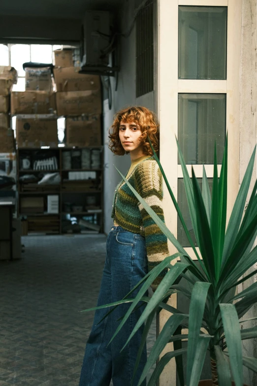 the young woman is posing near an indoor plant