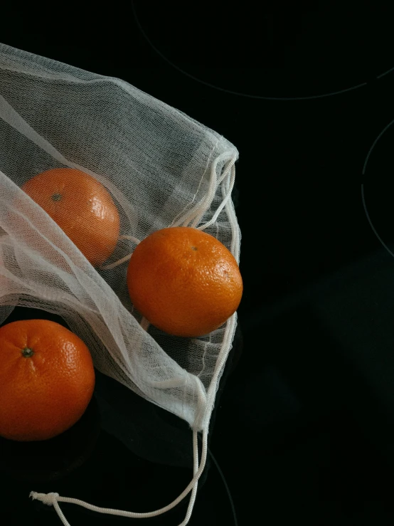 three oranges that are inside a net bag