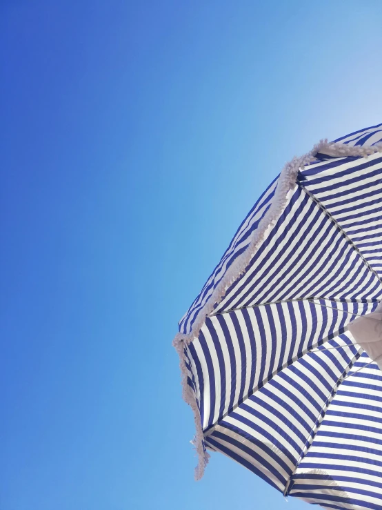 an open striped umbrella on the beach against a blue sky