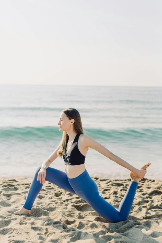 a young woman in blue pants doing a yoga pose on a beach