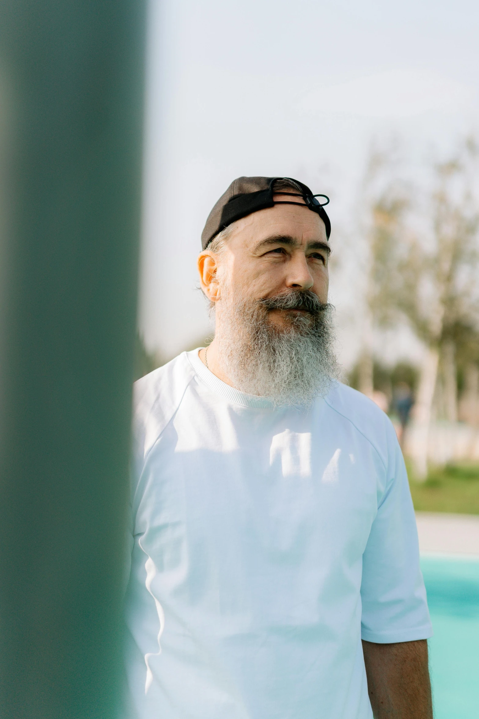 a man with a white beard and white t - shirt is standing by the pool