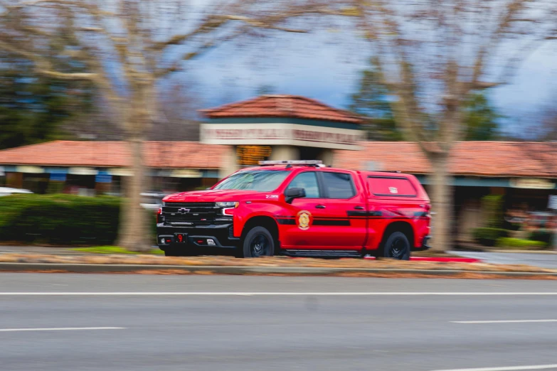 a red truck with its hood popped driving past some buildings