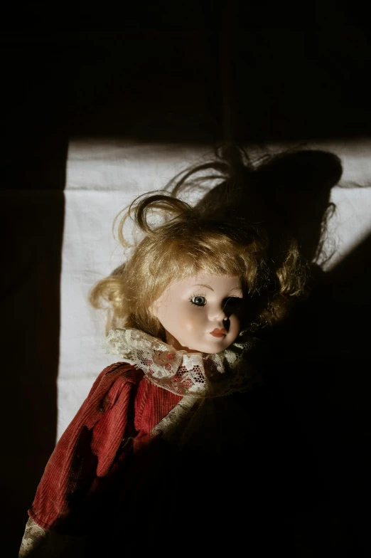 a doll with blonde hair is sitting in the shadows