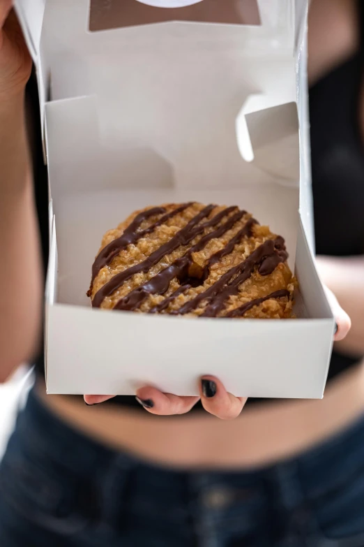 person holding up an open box with chocolate covered pastry