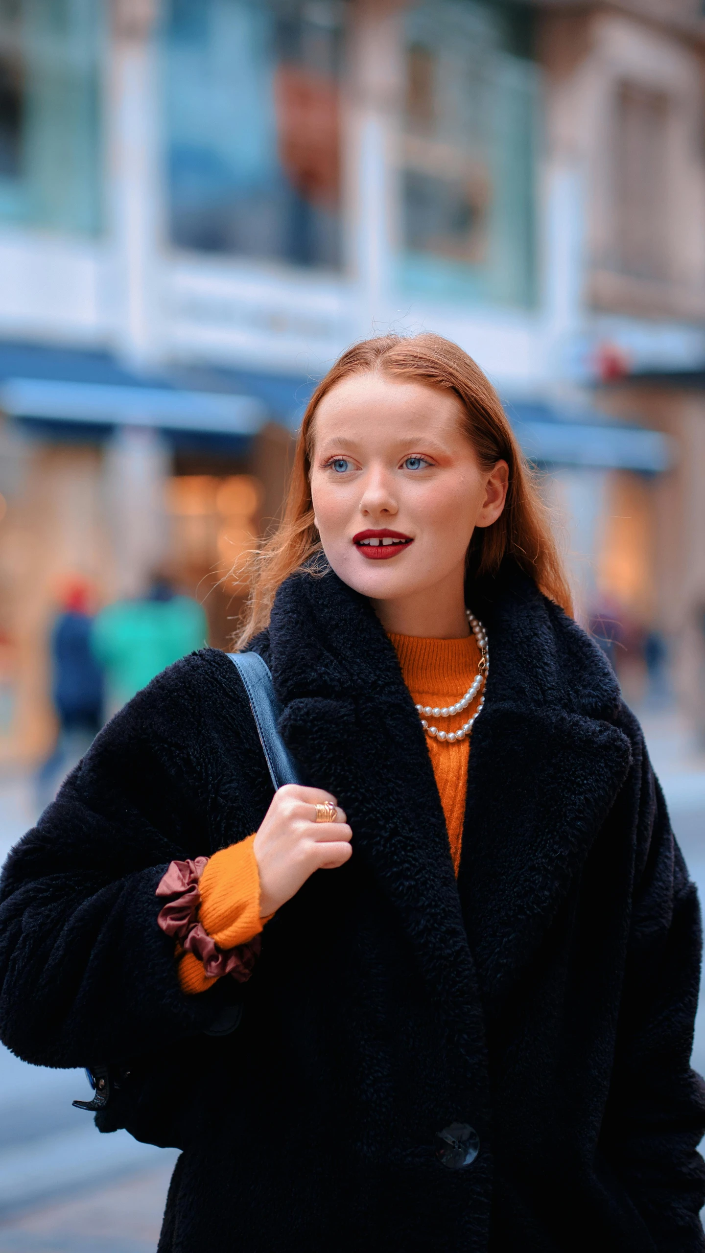 woman with red hair in black jacket standing near a building