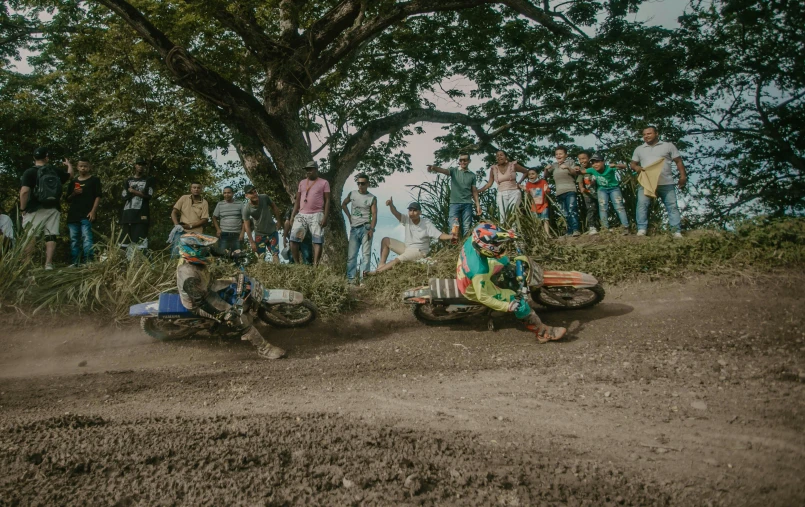 two people riding motorcycles in front of people in front of trees