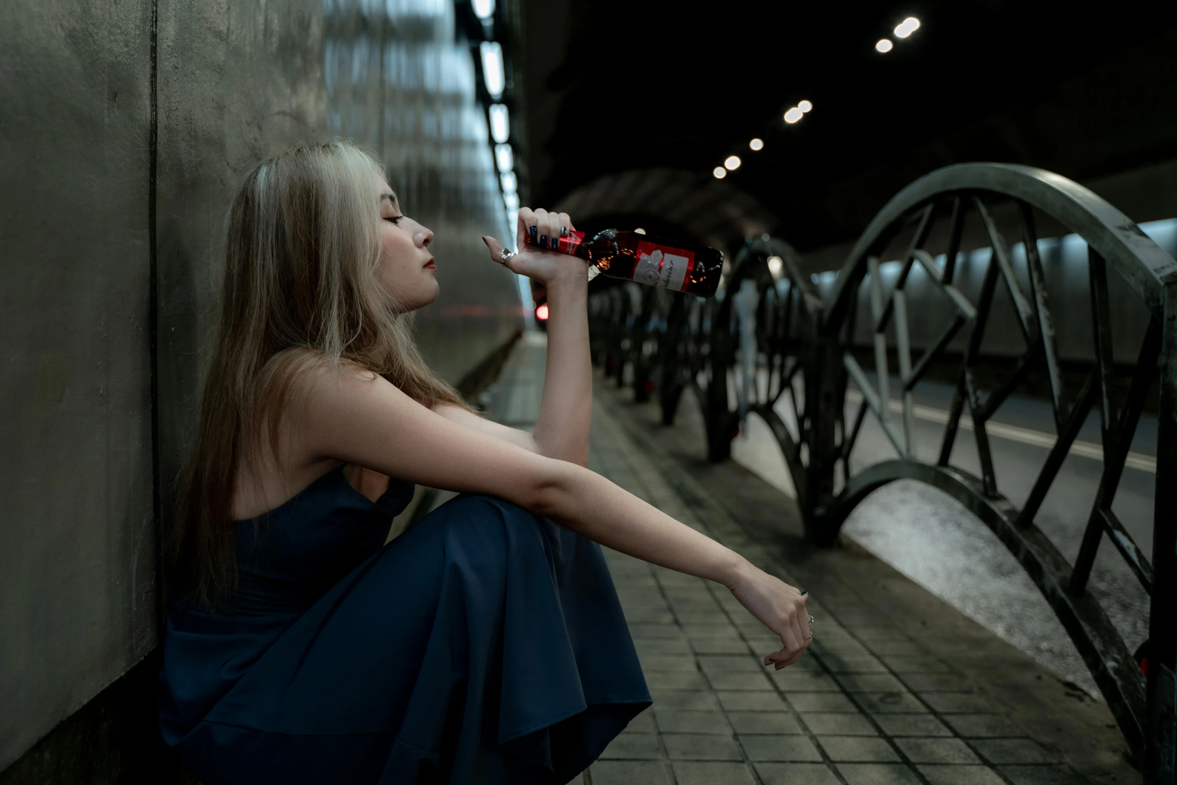 a girl leaning on a wall drinking from a bottle