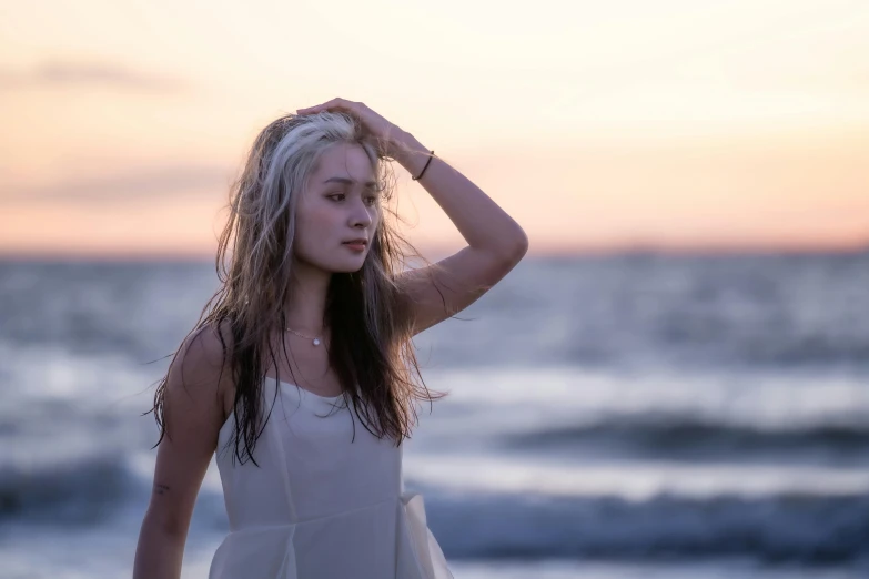 woman standing on the beach holding her head in one hand