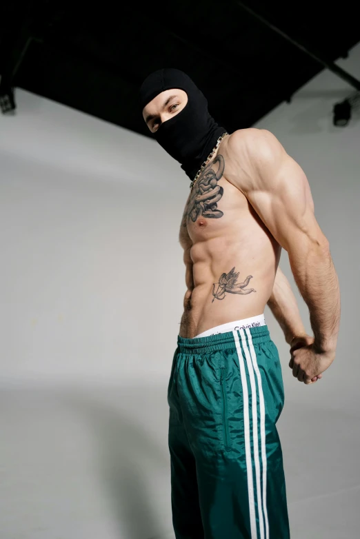 a man in a hat and sweat pants posing in front of a white backdrop
