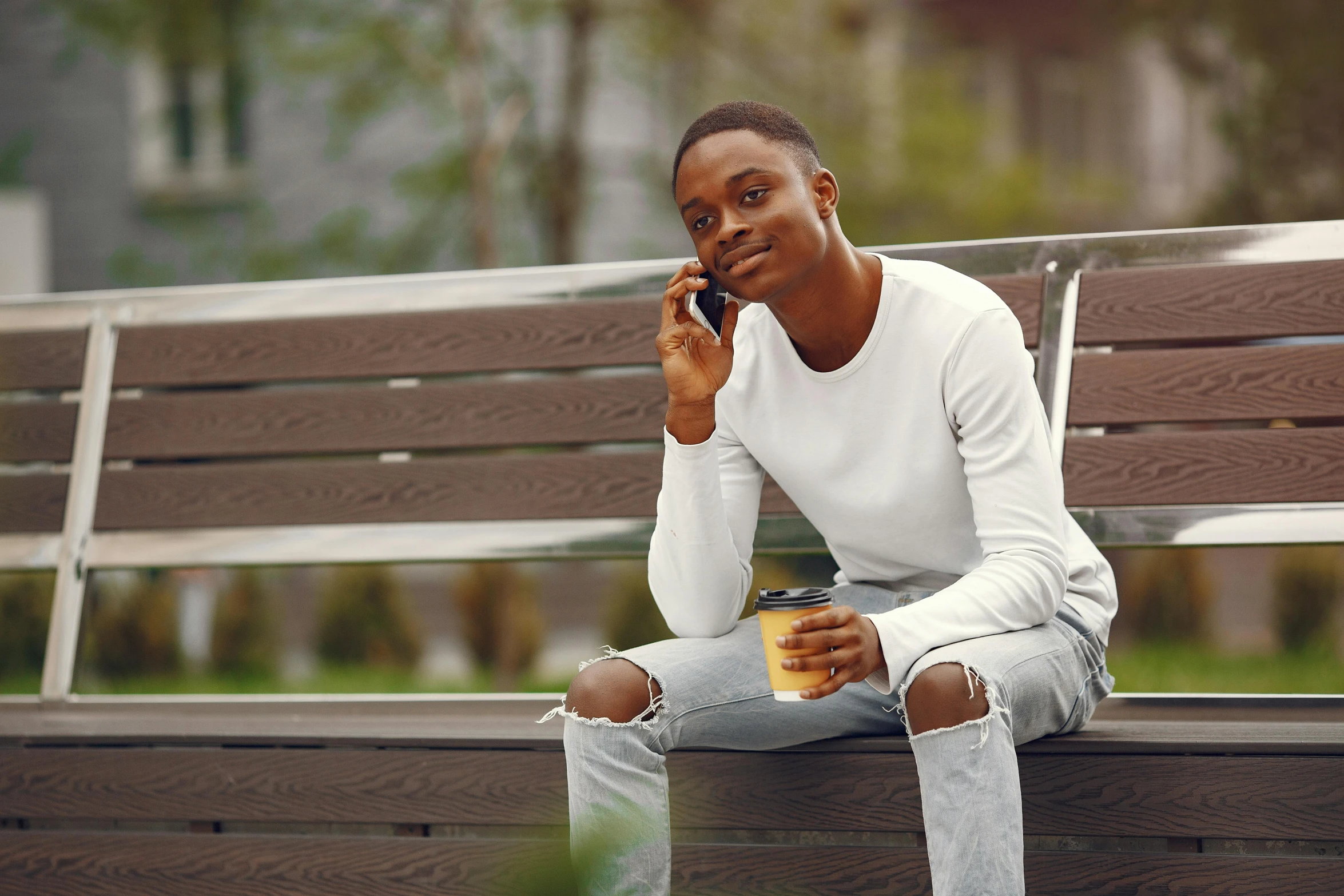 a man sits on a park bench while talking on his cell phone