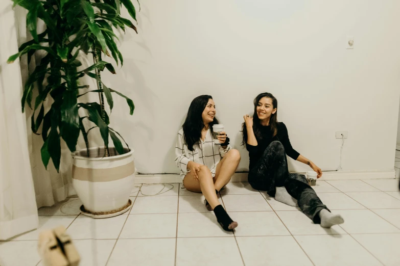 two young women sitting on the floor sharing coffee