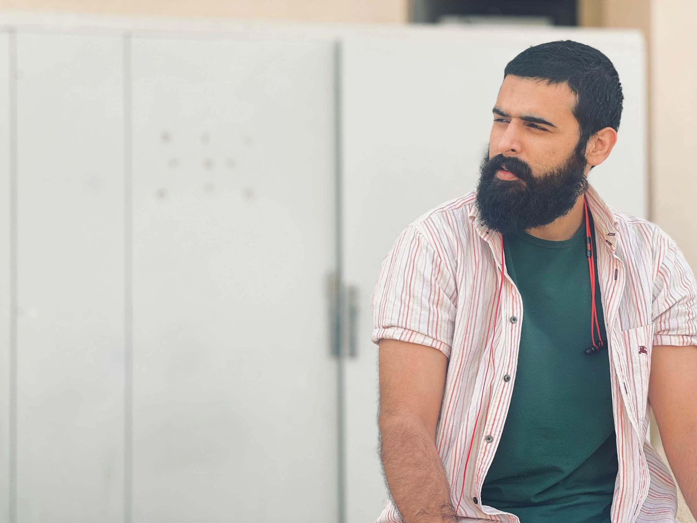 man with beard sitting by lockers looking away from camera