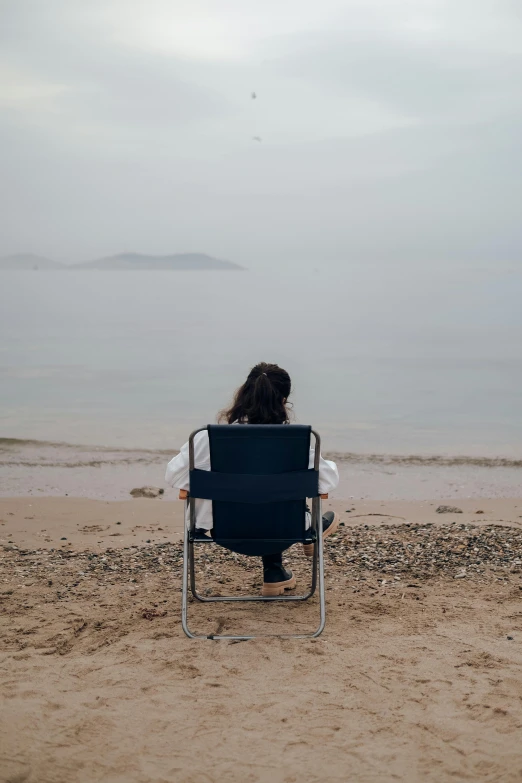 a person sitting on a beach in a chair near the water