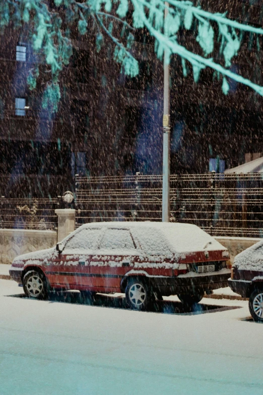 two cars covered in snow sit next to a parking meter