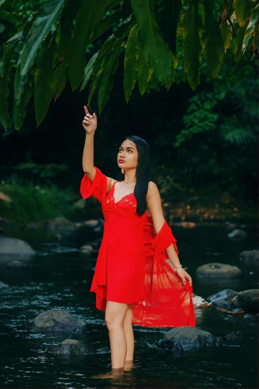 woman with red dress walking in stream looking up at trees