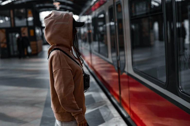 a person wearing a hoodie with one hand on a suitcase at a train station