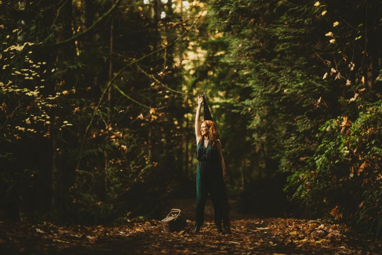 a woman standing in a forest with her hand up to the sky