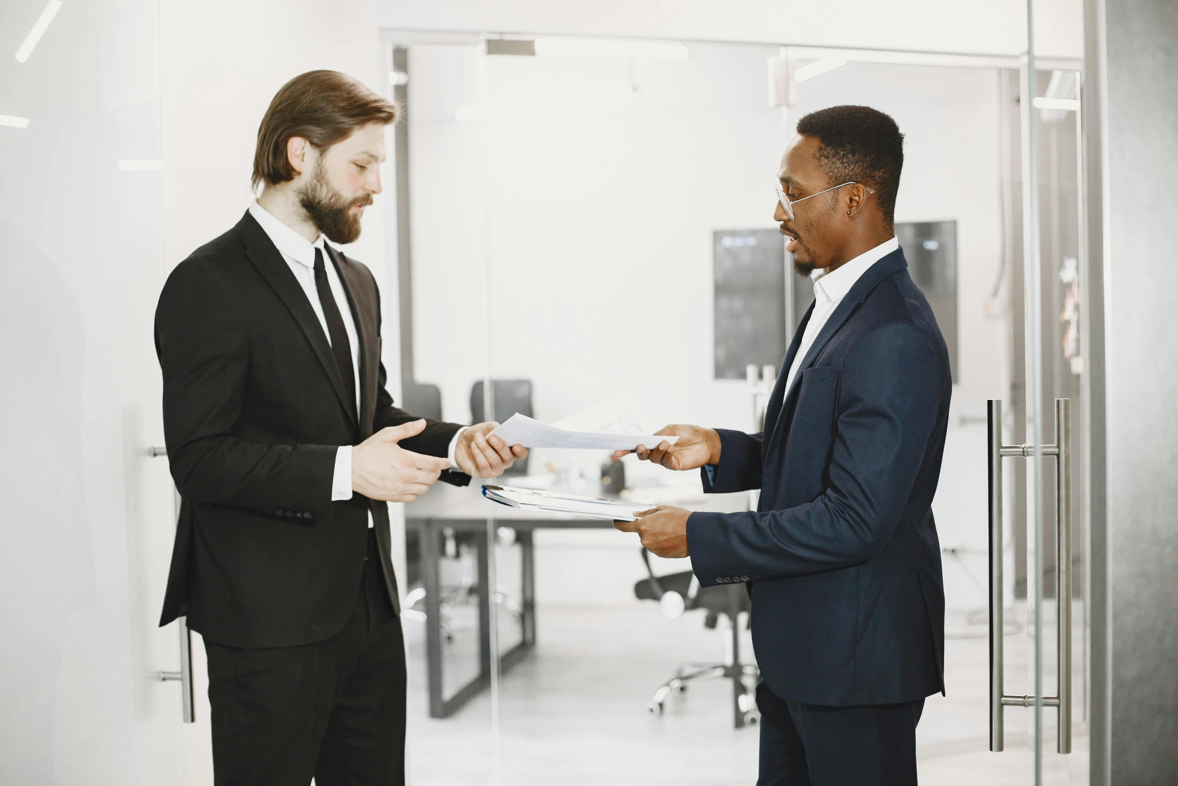 two men dressed in suits, one is looking at another while holding his hands together