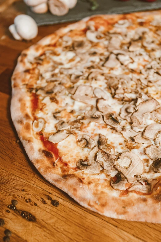 an old style cheese and mushroom pizza sits on a wooden table