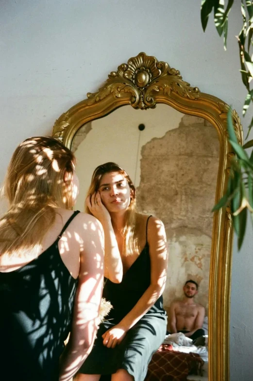 a beautiful young woman wearing black sitting in front of a mirror