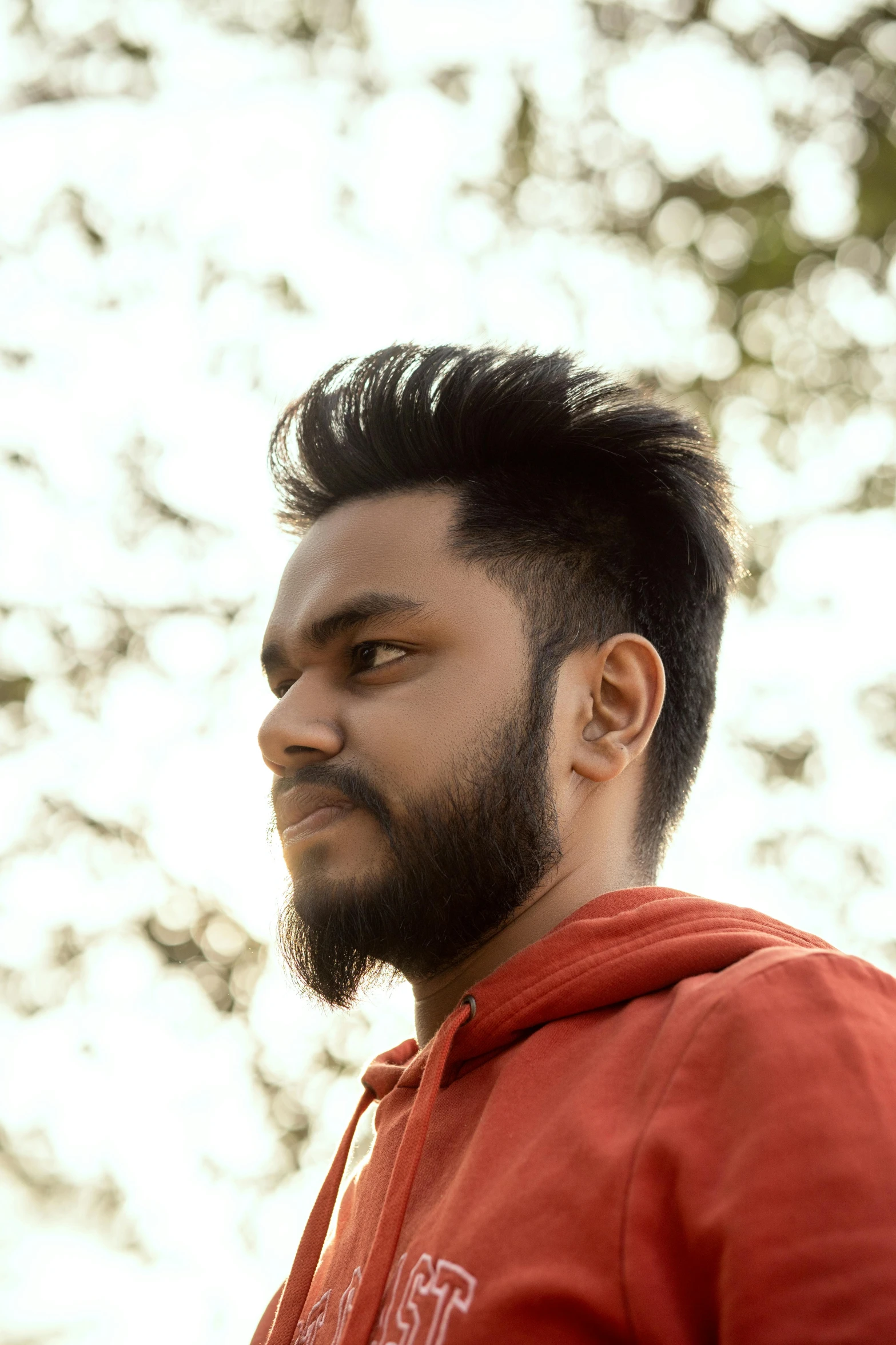 man with short dark hair wearing red sweatshirt looking to the left