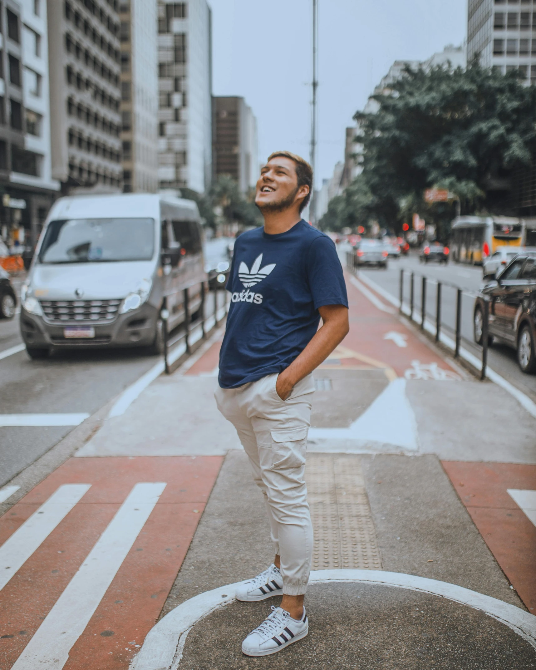 man in adidas t - shirt posing on crosswalk by city street