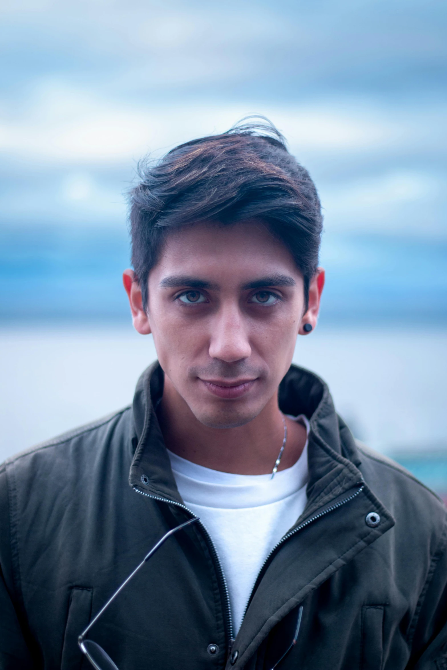 young man wearing white shirt and green jacket by the ocean