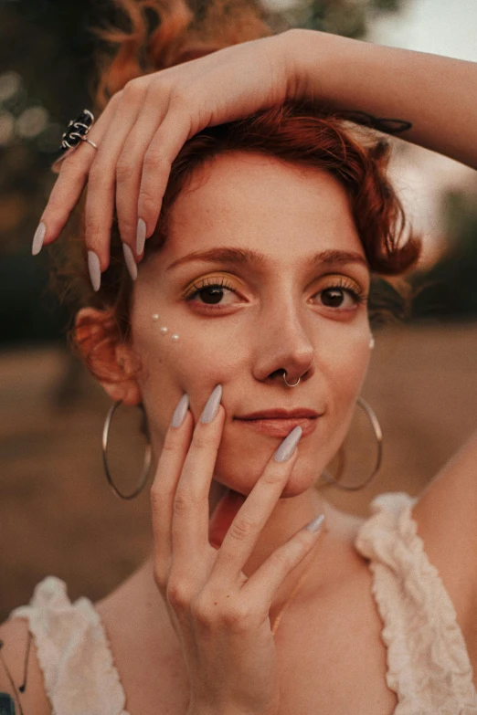 a woman with red hair and rings on her hand, and looking at the camera while she wears small earrings