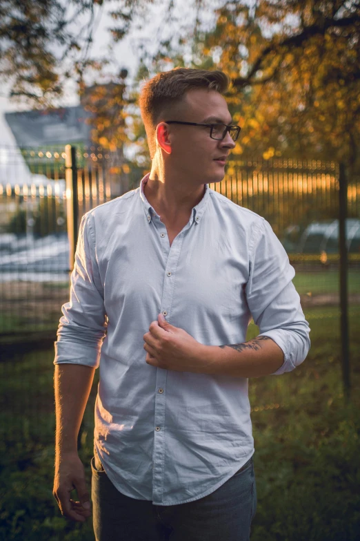 a man wearing glasses is posing in front of some trees