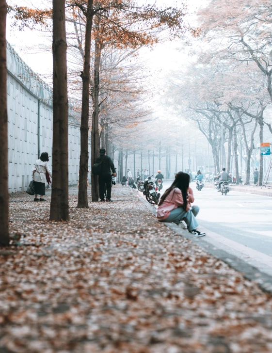 the girl crouches down in front of the tree on the sidewalk