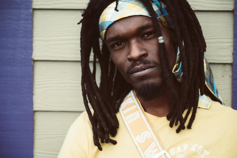 a man with dreadlocks stands by a house