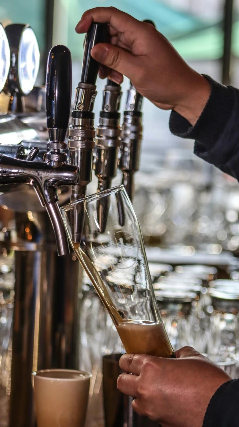 a person holding a beer near a tall machine filled with liquid