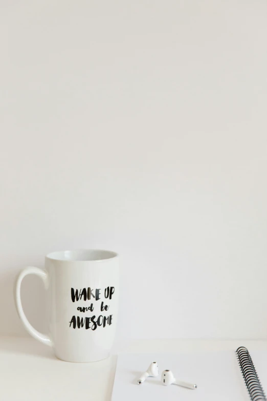 a white coffee mug and earbuds sit on a desk