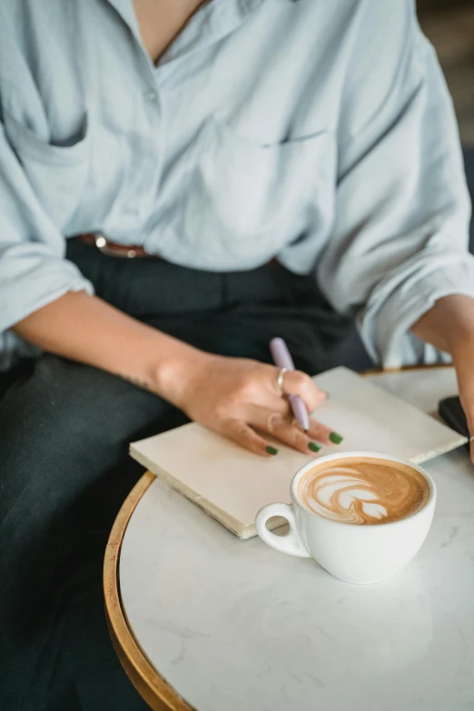 a woman writing in her notebook on a table with a coffee