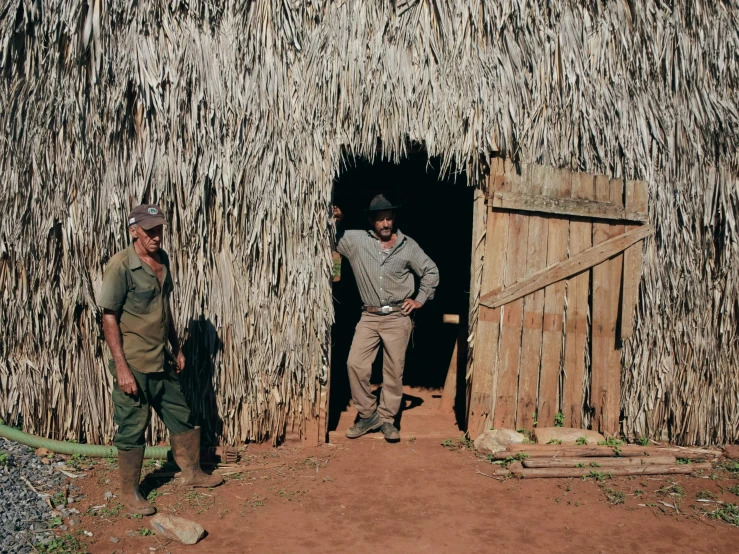 two people in front of a small shack with palm leaves