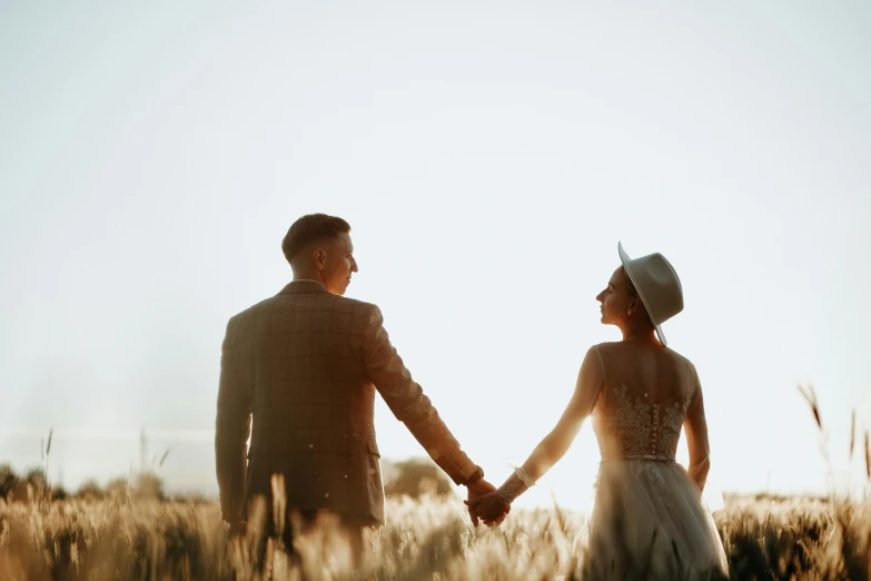 a couple holding hands and walking in a wheat field