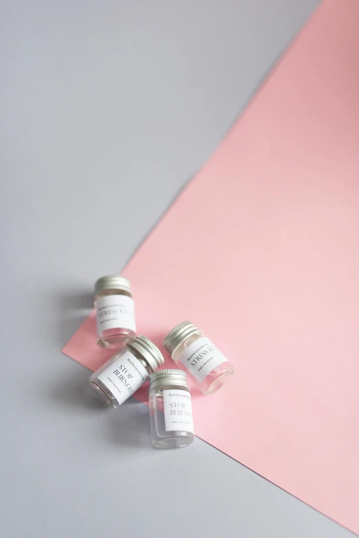 three jars with white labels on top and pink background