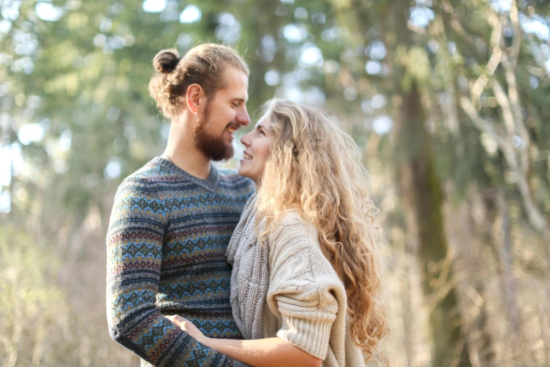 a woman with her hair id in the wind standing next to a man who is holding his hands around him