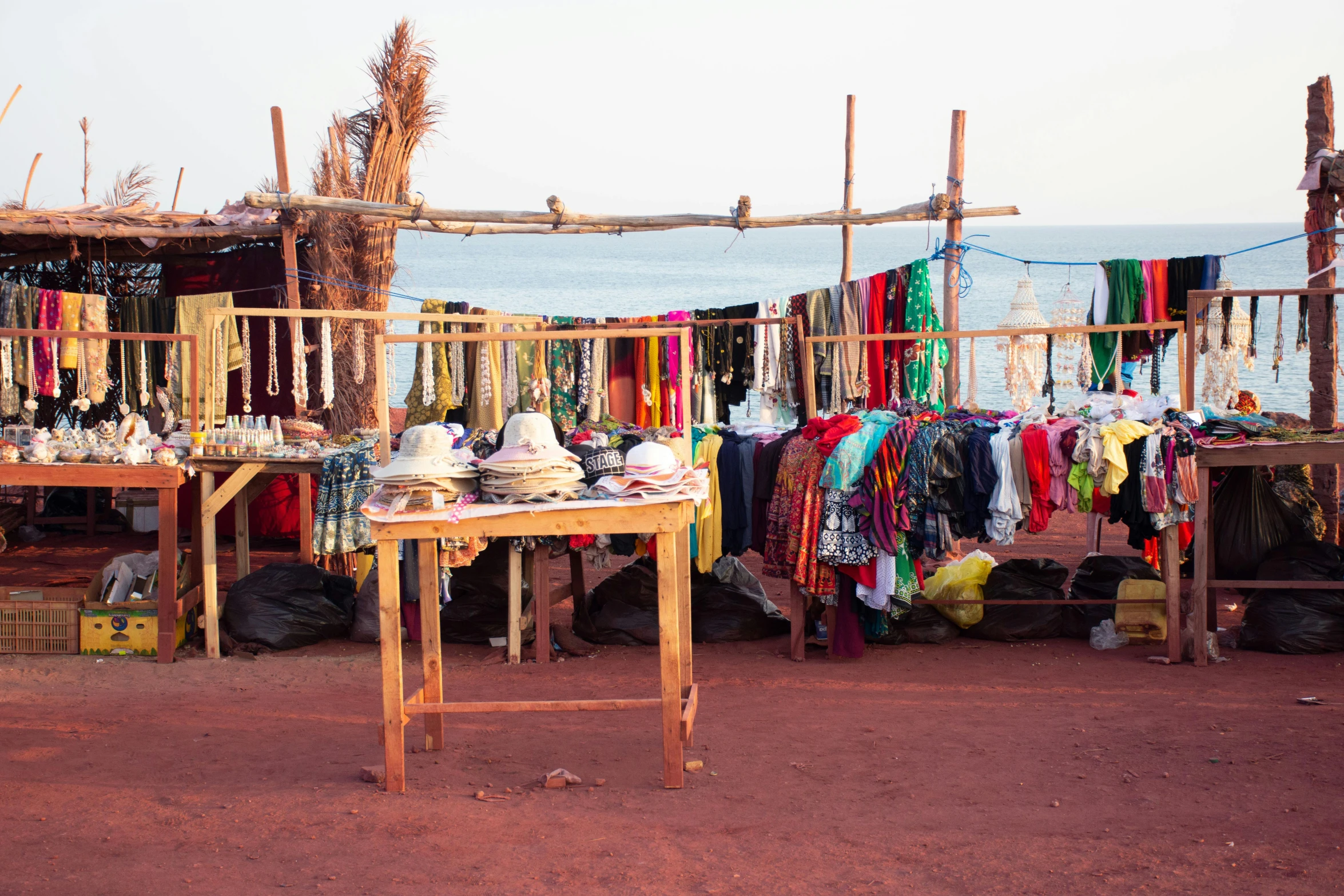 a market area by the water with clothing on tables and a store with clothes hanging