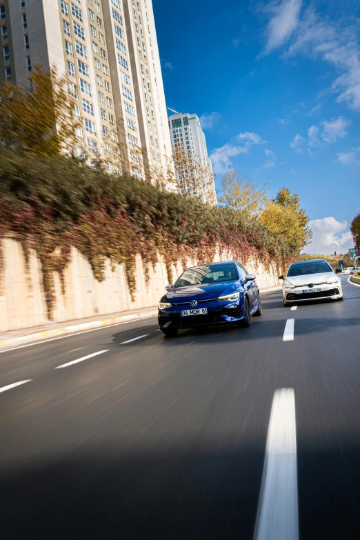 two cars driving down an open road in front of tall buildings