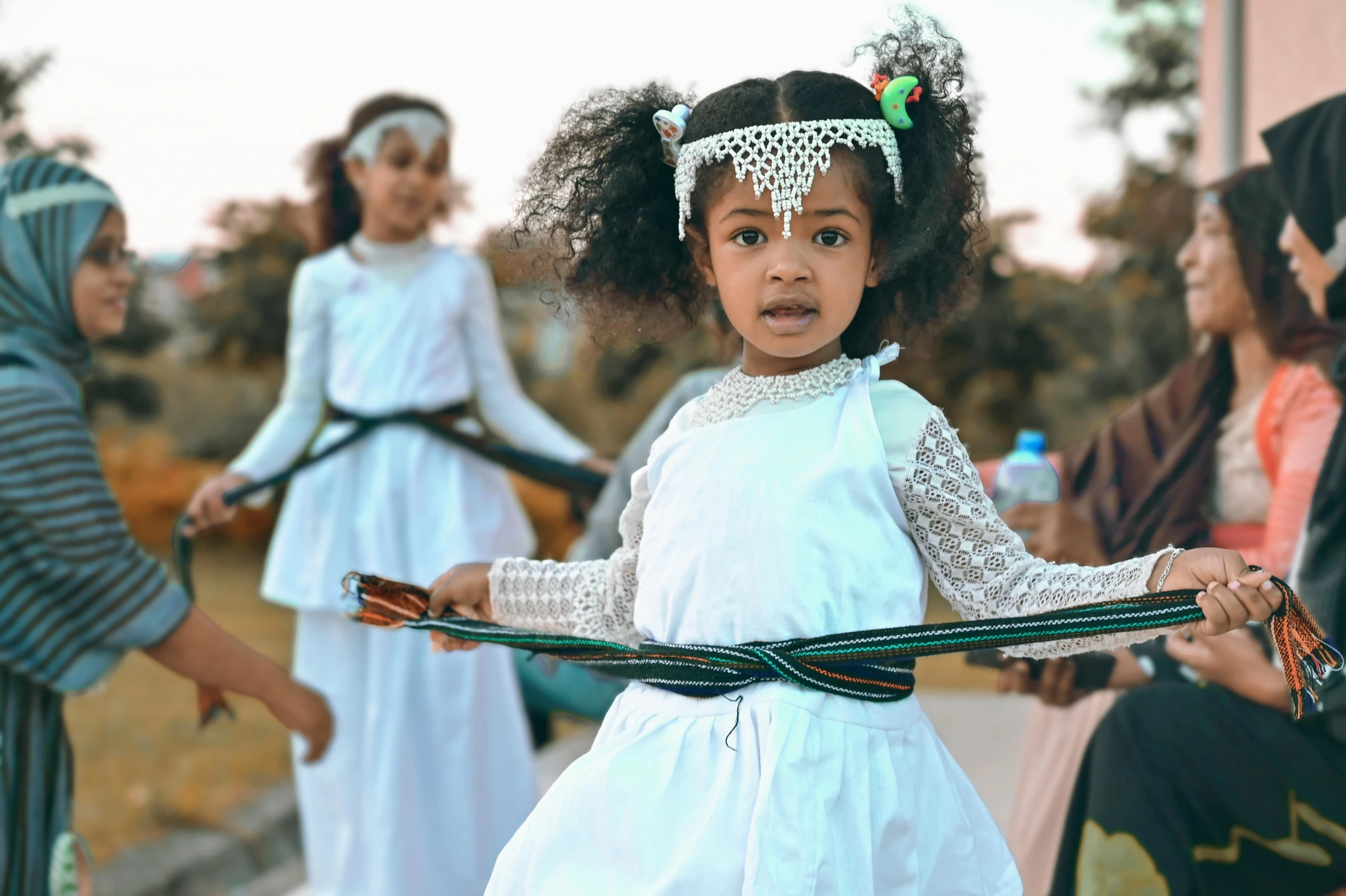 little girls in white dresses playing with a stick